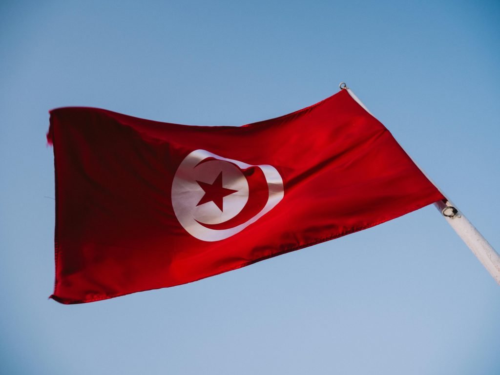 The vibrant red Tunisian flag with crescent and star against a blue sky.